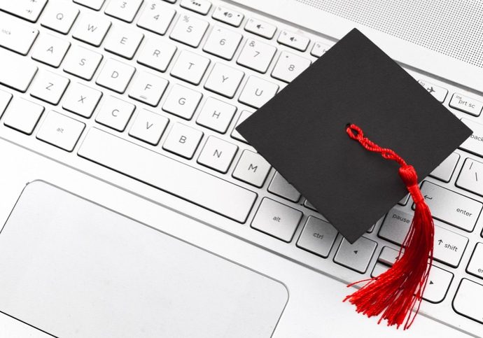 Internet academic learning, e-learning and online college education concept theme with close up on graduation cap with red tassel on computer keyboard with copyspace Internet academic learning, e-learning and online college education concept theme with close up on graduation cap with red tassel on computer keyboard with copy space