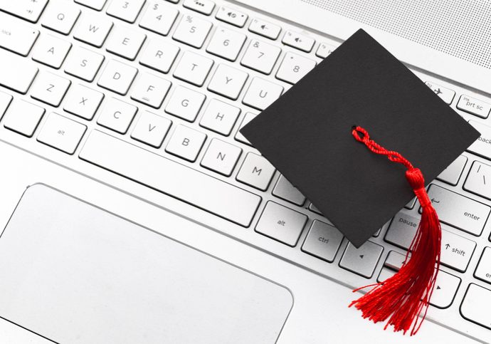 Internet academic learning, e-learning and online college education concept theme with close up on graduation cap with red tassel on computer keyboard with copy space