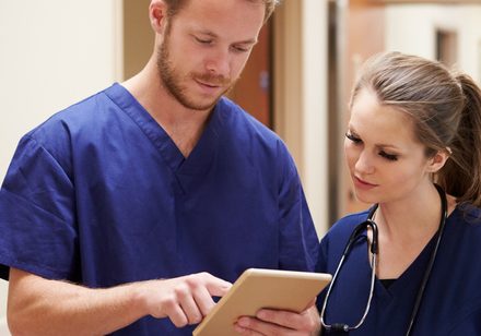 Medical Staff Looking At Digital Tablet In Hospital Corridor Medical Staff Looking At Digital Tablet In Hospital Corridor